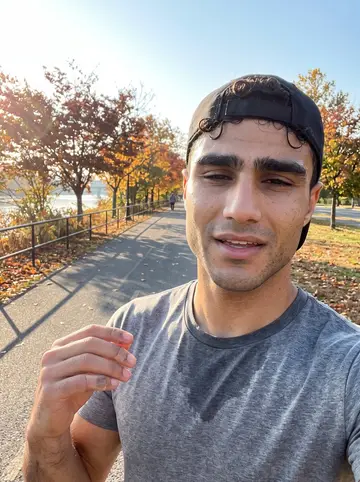Thiago, AI character: the Passaic riverfront path in Riverbank Park after an early run, orange trees behind