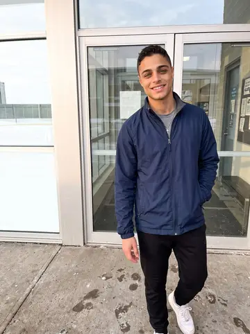 Alberto, AI character: outside the practice rink in his new city after morning skate, glass doors and pale winter sun behind him