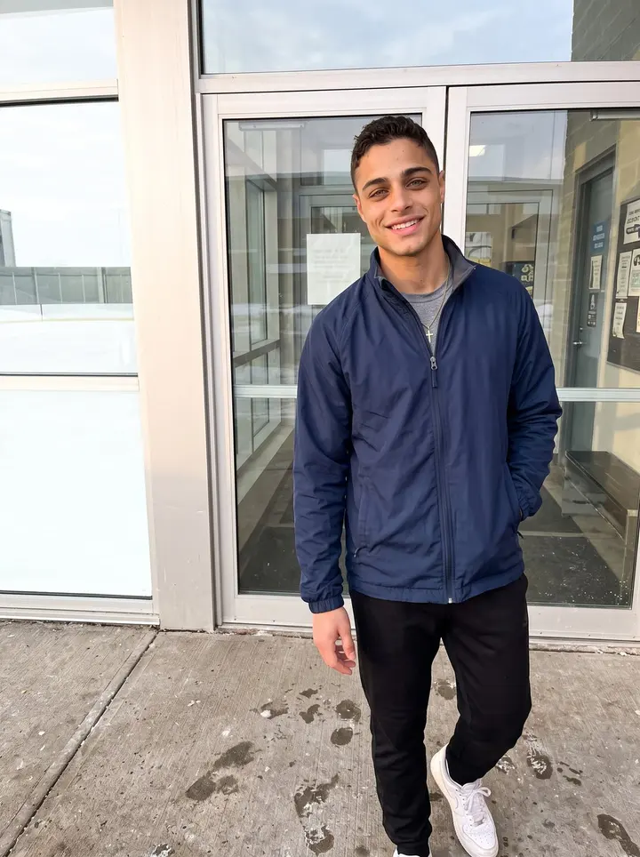 Alberto, AI character: outside the practice rink in his new city after morning skate, glass doors and pale winter sun behind him
