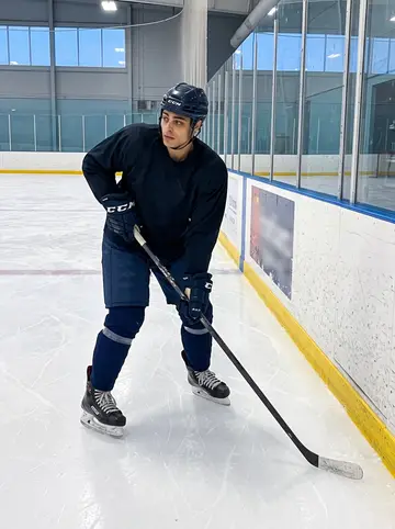 Alberto, AI character: inside the hockey rink during an open practice, boards and scratched ice visible around him