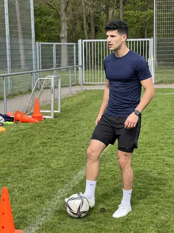 Julio, AI character: club training ground during morning drills, cones and a small goal behind him