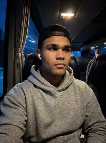 Brandon, AI character: back row of the team bus during a long overnight road trip, dark highway glass behind him