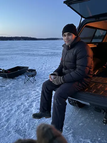Brandon, AI character: frozen lake north of Minneapolis with an ice-fishing sled, thermos and small folding chair beside a pickup…