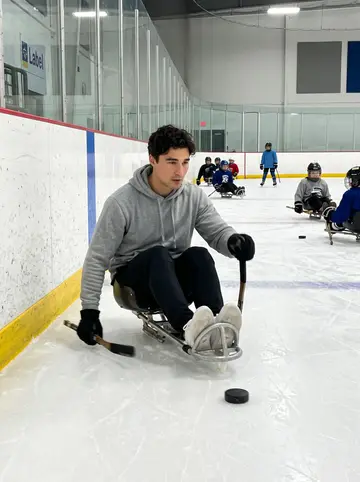 Evan, AI character: inside a community ice rink during Tuesday night sled hockey practice, low boards and sleds on the ice
