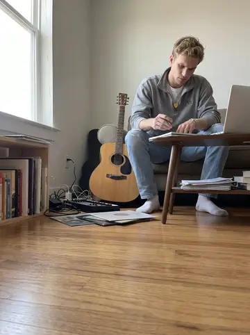 Andrew, AI character: his apartment music corner in Nashville, laptop open for a FaceTime piano lesson, acoustic guitar on his…