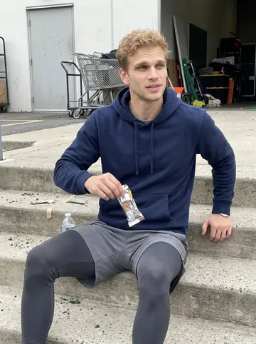 Andrew, AI character: concrete steps outside the team practice facility, equipment carts and a plain metal door in the background