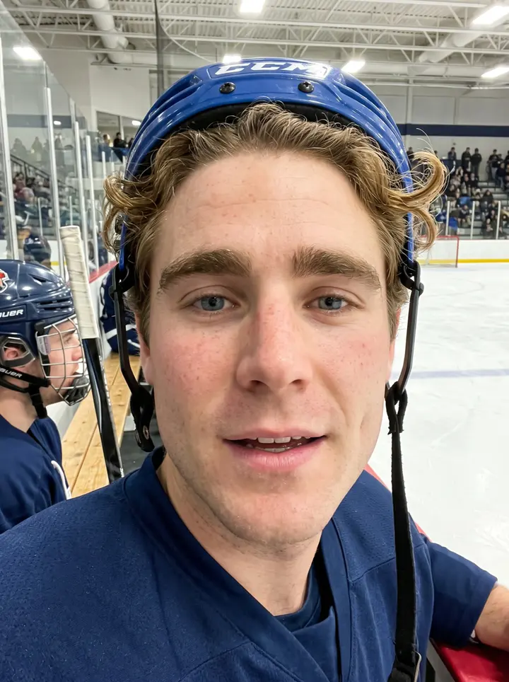 Alasdair, AI character: outside the university rink after afternoon practice, leaning against the dark rink boards with snowbanks…