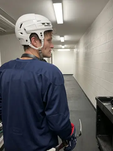 Danylo, AI character: inside a road arena during a late practice, boards and empty lower seats visible behind the glass