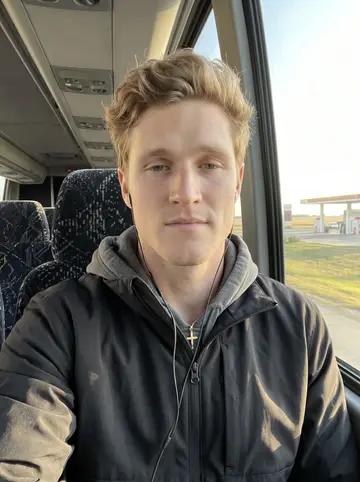 Danylo, AI character: team bus window seat on the way to an away game, flat prairie fields and a gas station sliding past outside