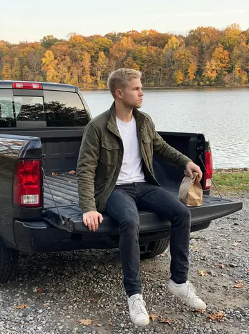 Bjørn, AI character: a quiet lake pull-off north of the Twin Cities, his pickup parked near the water with a paper lunch bag…