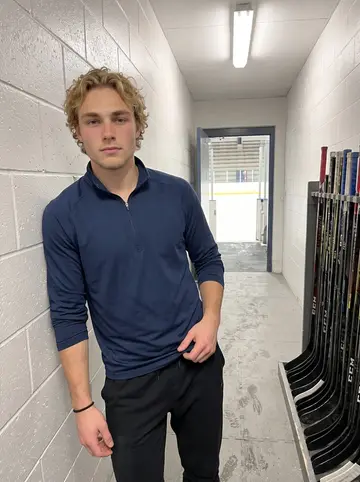 Teddy, AI character: the concrete tunnel behind the bench at Cheel Arena after a home game, sticks racked on the wall