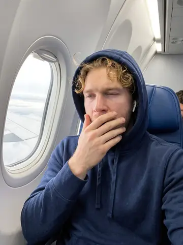 Brody, AI character: a window seat on the team's early flight to a road game, grey clouds outside