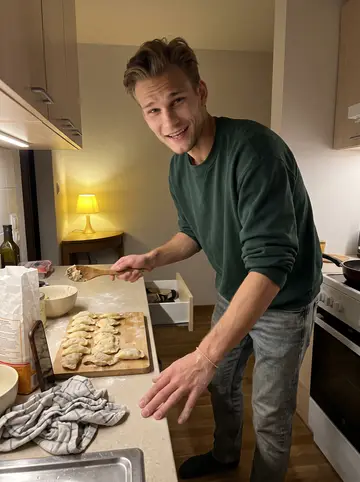 Tomasz, AI character: small rented apartment kitchen after evening training, flour on the counter and uneven pierogi on a…