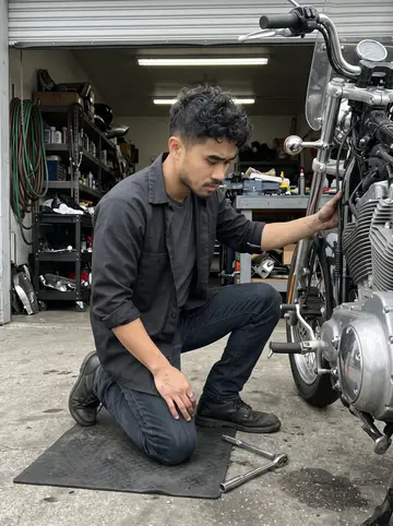 Paolo, AI character: the service bay of a small Daly City motorcycle garage, tools on a rolling cart and a half-open garage…