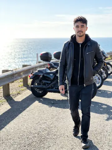 Paolo, AI character: a roadside stop above Pacifica after a short winter ride, ocean visible beyond parked motorcycles