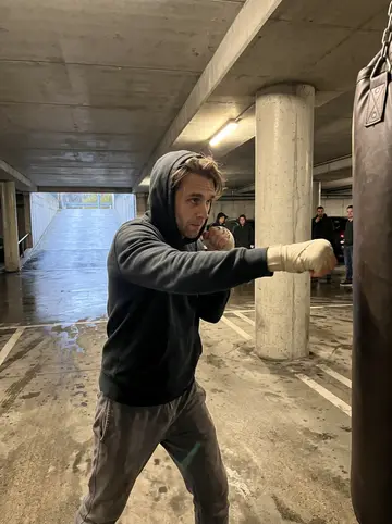 Jules, AI character: underground parking garage beneath a closed supermarket in Lyon on Saturday fight night, concrete pillars…