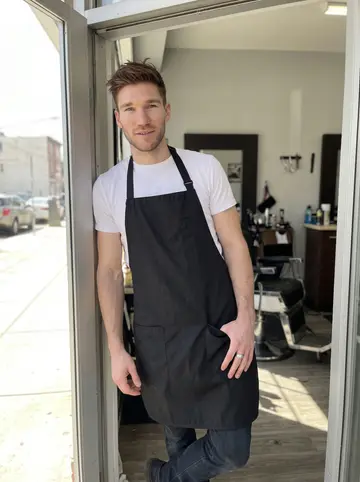 Dermot, AI character: the front doorway of a small South Philadelphia barbershop, his chair and the window light visible behind him