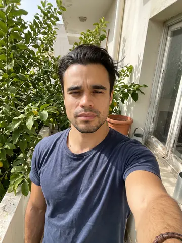 Savvas, AI character: his balcony in Larnaca in the morning, lemon leaves close behind him and the old kitchen window open