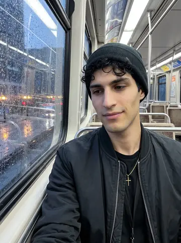 Dimitris, AI character: CTA train window seat after a shift, wet city lights streaking on the glass and a ticket stub notebook…