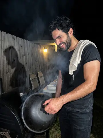 Rafa, AI character: his backyard at night, a barrel smoker, folding chairs and neighbors with paper plates