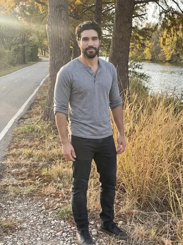 Rafa, AI character: the Mission Reach trail along the San Antonio River in late afternoon, tall grass and the river behind