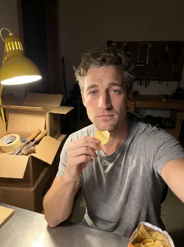 Bo, AI character: the cold cabinet shop, a walnut tabletop clamped to the bench, hand planes and chisels on the wall behind him