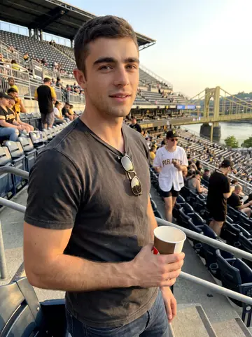 William, AI character: upper seats at PNC Park during a Pittsburgh Pirates game, yellow bridge and river visible beyond the rail