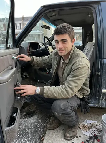 William, AI character: his cold driveway on a clear winter Sunday, the 1989 Ford pickup door open while he cleans the dashboard…