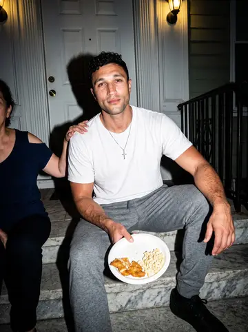 Kane, AI character: the marble front stoop of his mother's East Baltimore rowhouse on a hot night, a paper plate of food on…