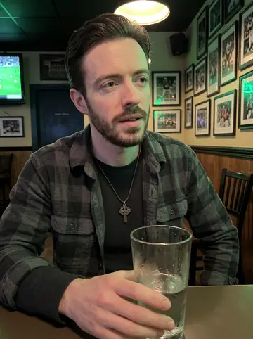 Flynn, AI character: a small Southie bar during a Celtics game on the radio, green bar lights and old framed sports photos on…