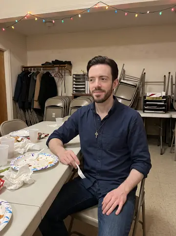 Flynn, AI character: a church hall in South Boston after his mother's November birthday dinner, folding tables and warm string…