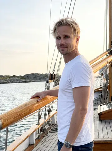 Ivar, AI character: on the deck of a borrowed 1970s wooden sailboat in the southern Gothenburg archipelago, one hand resting…