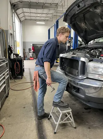 Carlos, AI character: inside the service bay at the Beaumont truck shop, beside a raised diesel pickup with the hood open