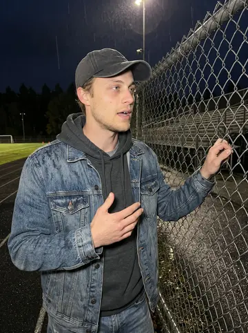 Carlos, AI character: at the fence of a Beaumont high school football field on a damp Friday night, bleachers and field lights…