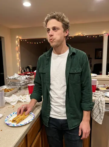 Carlos, AI character: his mother's kitchen during Christmas tamale night in Beaumont, foil trays and string lights on the counter
