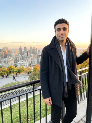 Karim, AI character: the Mount Royal lookout in Montreal near sunset, city buildings soft in the distance below the railing