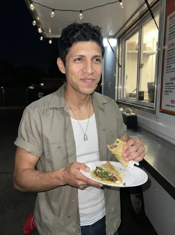 Raúl, AI character: standing by a taco truck counter under string lights after finishing a lettering job
