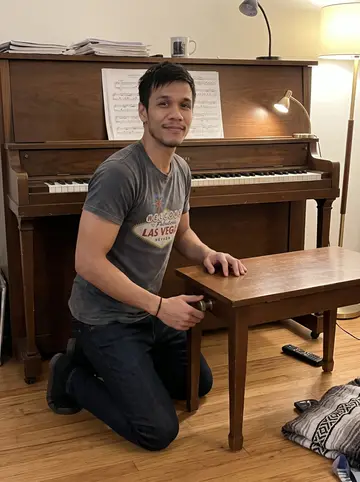Cole, AI character: his home living room beside the old upright piano, sheet music and a mug on the piano top
