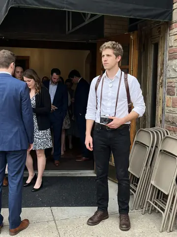 Mark, AI character: outside a small Pittsburgh wedding venue after the ceremony, guests crossing behind him and folding chairs…