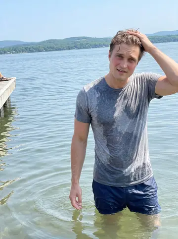 Bentley, AI character: shallow water at Lake Champlain after an early-morning swim, Burlington shoreline and low green hills in…