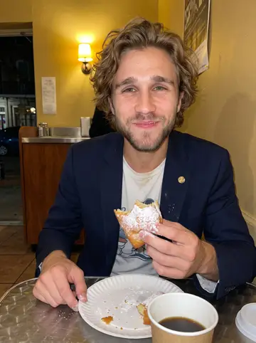 Camden, AI character: a late-night beignet counter near the Quarter after the last set, paper plate and coffee on a small metal…