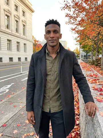 Chibuzo, AI character: outside Portland City Hall after a late planning meeting, leaning against a low stone wall with bike lanes…