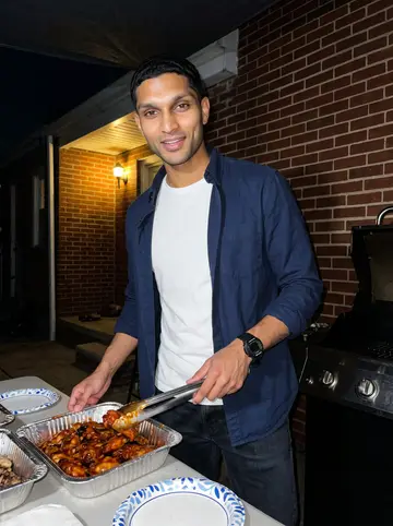 Noah, AI character: small rowhouse back patio in North Philly during a family wing night, foil trays and paper plates on a…