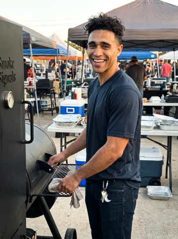 Rashid, AI character: a Houston barbecue cook-off lot at golden hour, standing beside the Smoke Signals smoker with folding…