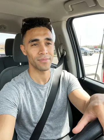 Rashid, AI character: parked at a Texas gas station on the way to a barbecue cook-off, borrowed truck cab, highway sun through…