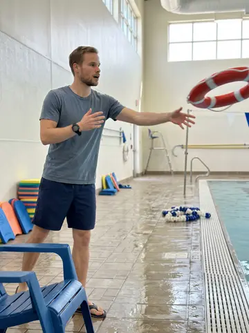 Danny, AI character: Saturday adult water-safety class at the community pool in Astoria, lane ropes and kickboards behind him