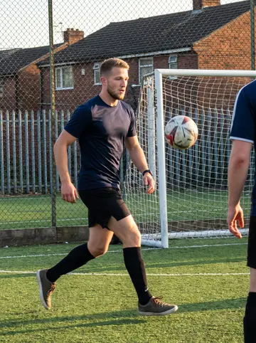 Alfie, AI character: a five-a-side football pitch in Salford after work, chain-link fence and low brick houses beyond it