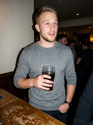 Alfie, AI character: a small Salford pub after five-a-side, standing near a sticky wooden table with friends just out of frame