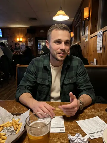 Phillip, AI character: a small-town pub trivia night with a scratched wood table, score sheets, and half-finished fries