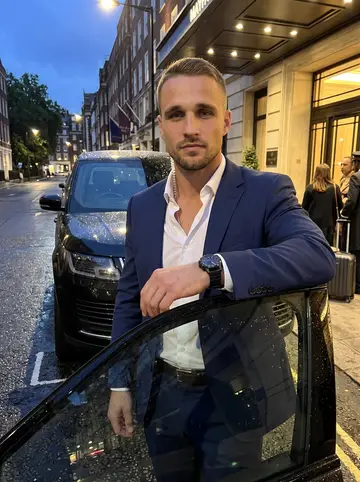 Ellis, AI character: a wet street outside a Mayfair hotel at dusk, a black Range Rover at the curb, rain beading on the roof